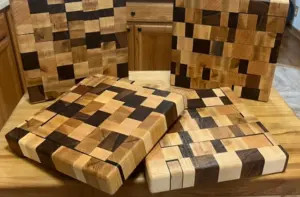 Several checkerboard-patterned end-grain cutting boards in light and dark wood, stacked and leaning on a kitchen counter