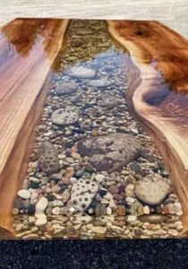 Live-edge wood serving board with a clear resin river inlaid with beach stones running down the center